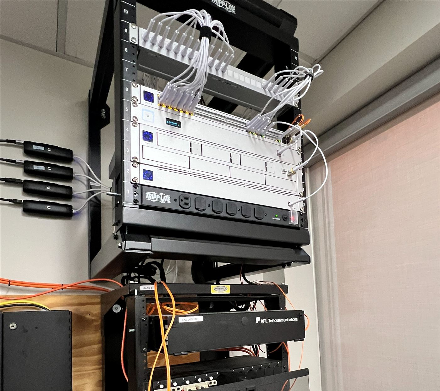 Wall-mounted network rack with switches, patch cables, a surge protector, and a labeled fiber enclosure below
