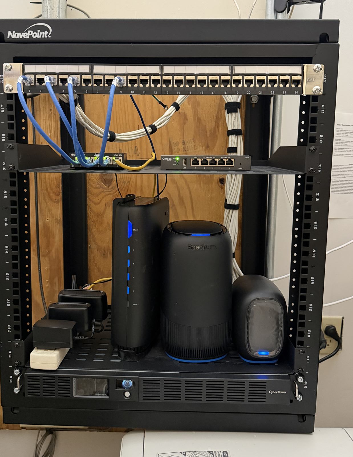 Wall-mounted network rack with a 24-port patch panel, router, switch, and battery backup