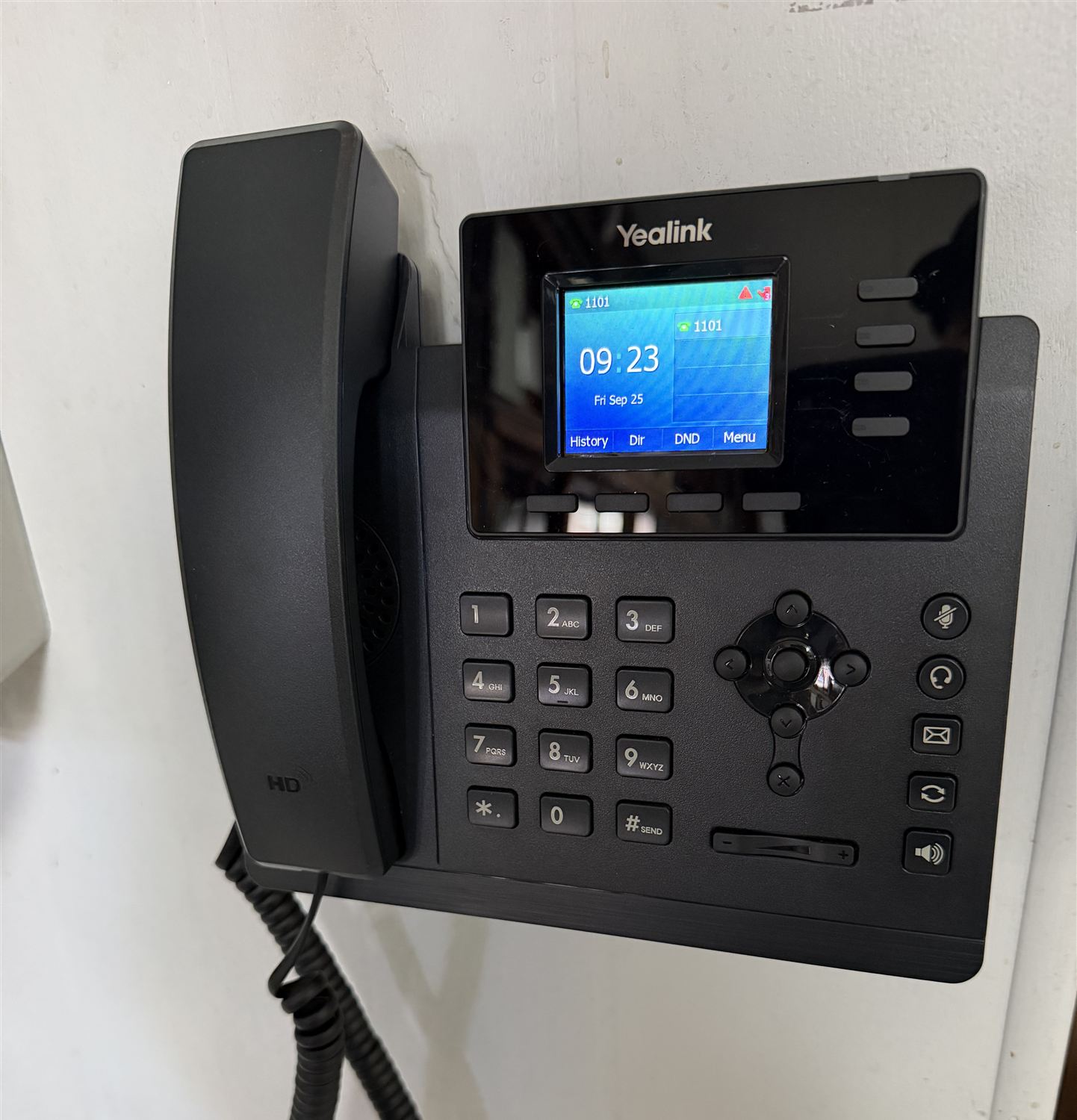 Yealink color-screen IP phone mounted on a wall, showing extension 1101 and the date